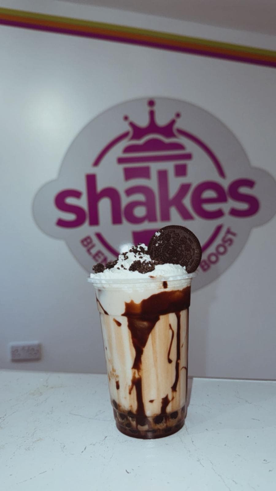 Oreo milkshake with chocolate drizzle and Oreo cookie in front of the Shakes Gravesend logo